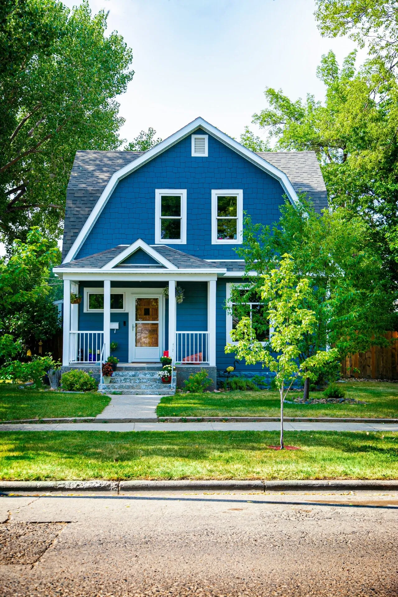 A blue two-story house with white trim and a front porch, surrounded by green trees