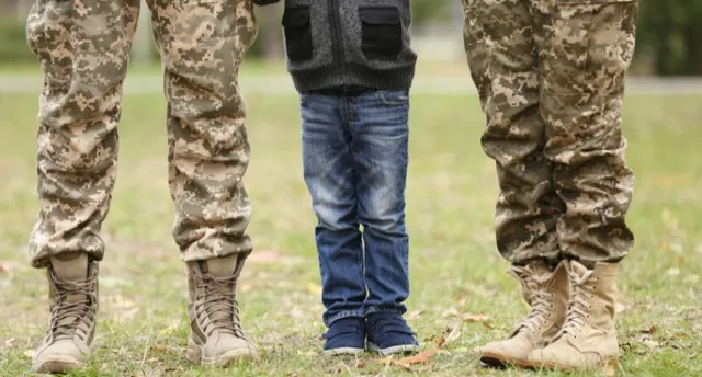 Legs of male and female military service members with child between them on grass, representing dual income home buying power.